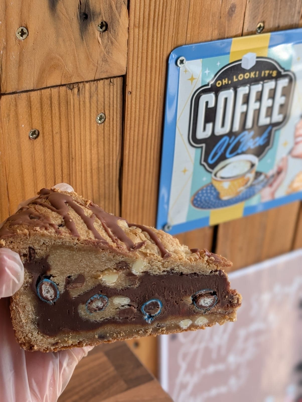 Chocolate chip cookie bar held up showing fudgy layers, with a Coffee O'Clock tin sign in the background