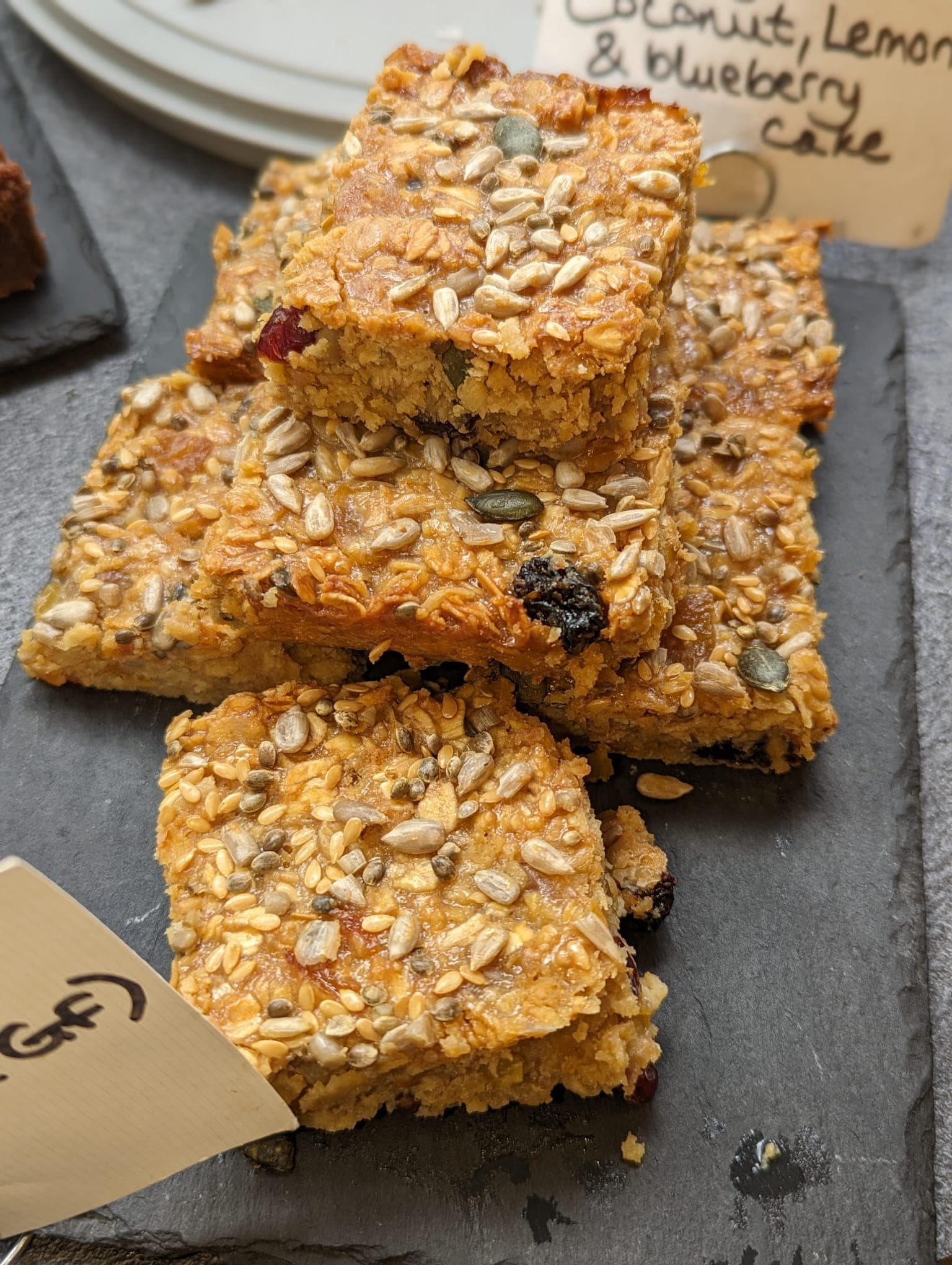 Stack of seeded gluten-free flapjacks on a slate with a handwritten label