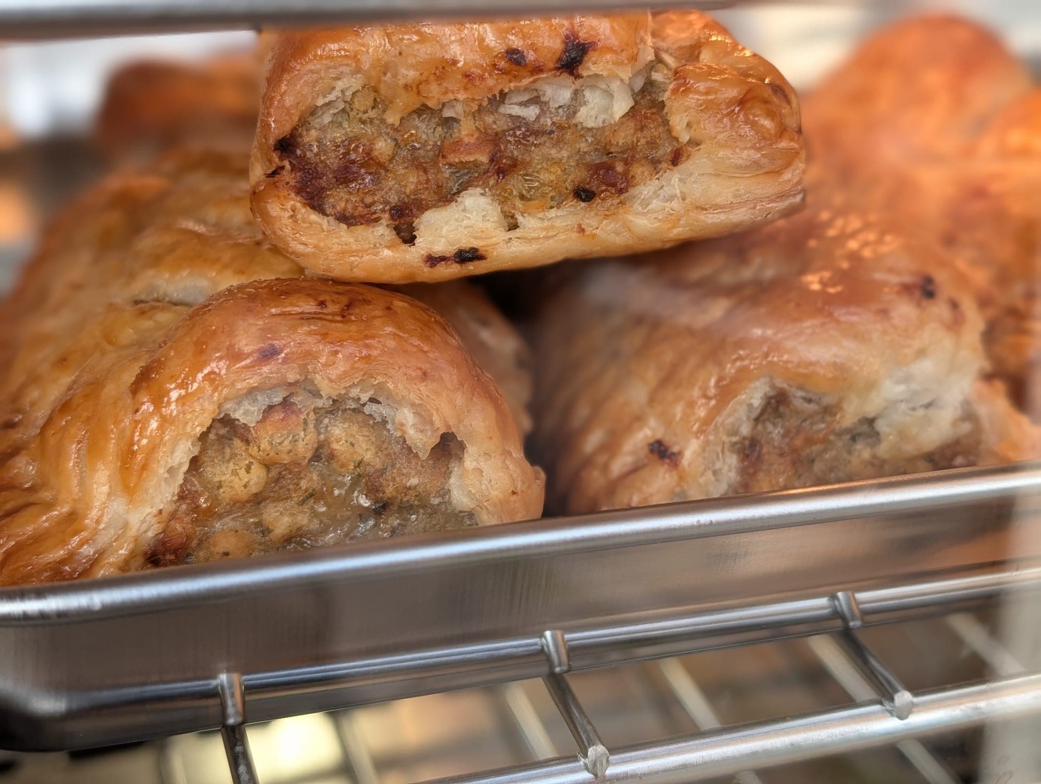 Freshly baked golden sausage rolls in a metal tray, one broken open to show the filling
