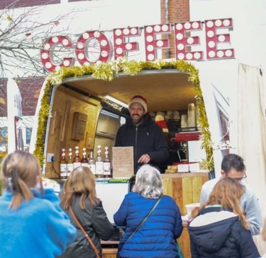 Ahh Roma barista in a Santa hat serving customers at a decorated Christmas market stall