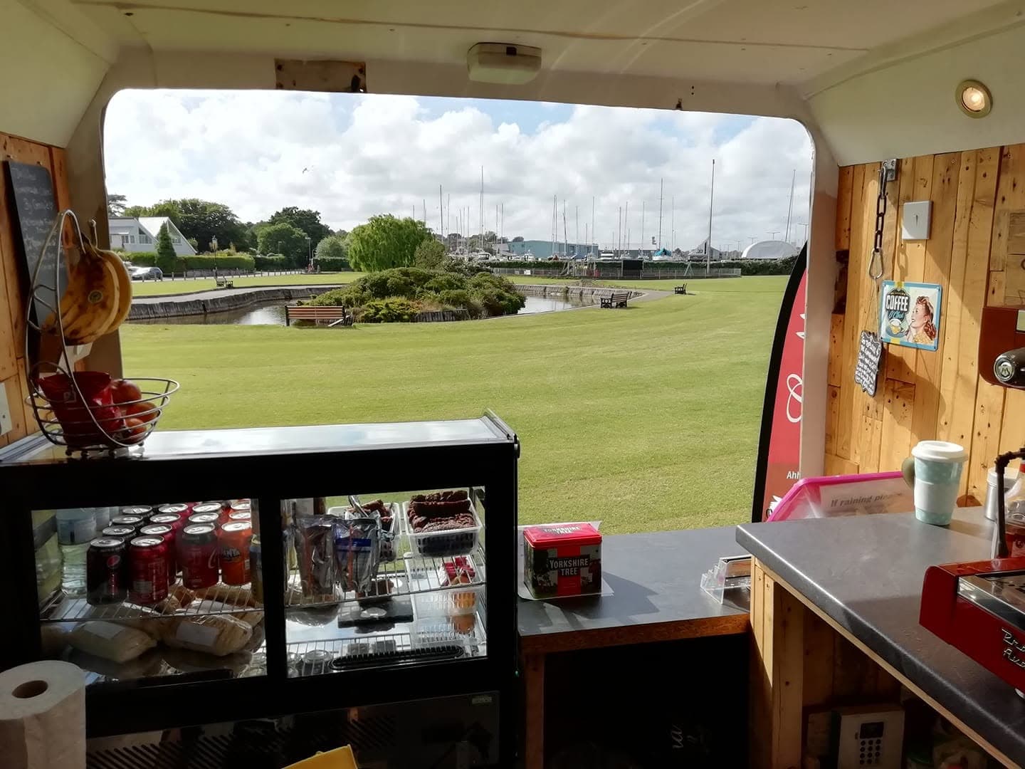 View from inside the coffee van looking out over a green and marina at golden hour