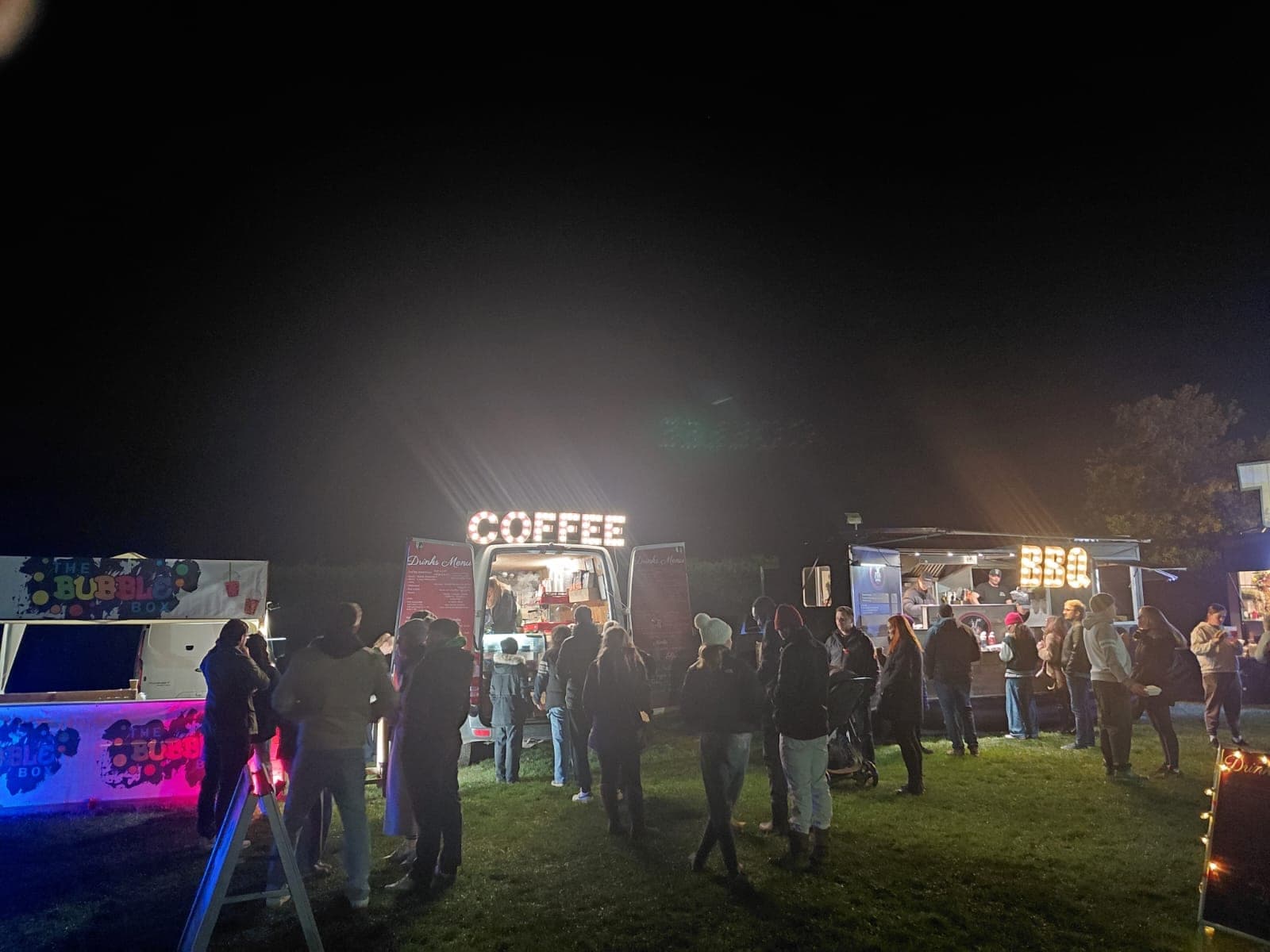 Crowd gathered at a night event around the lit Ahh Roma COFFEE van alongside BBQ and other food stalls