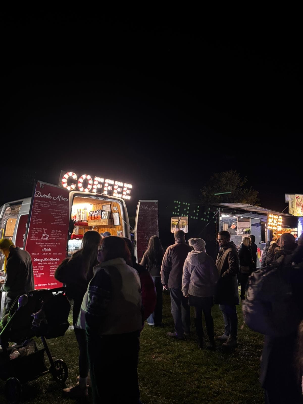 Evening event crowd around the Ahh Roma van with illuminated COFFEE sign, other stalls glowing in the dark
