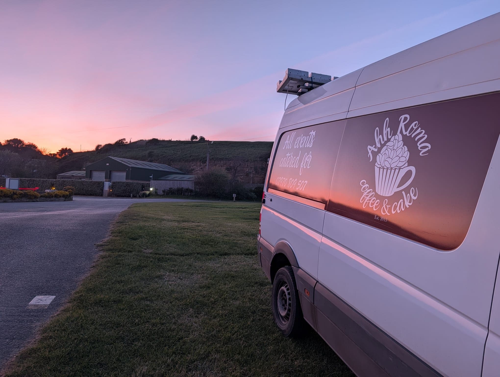 The Ahh Roma coffee van with branding lit by a pink and purple sunset sky